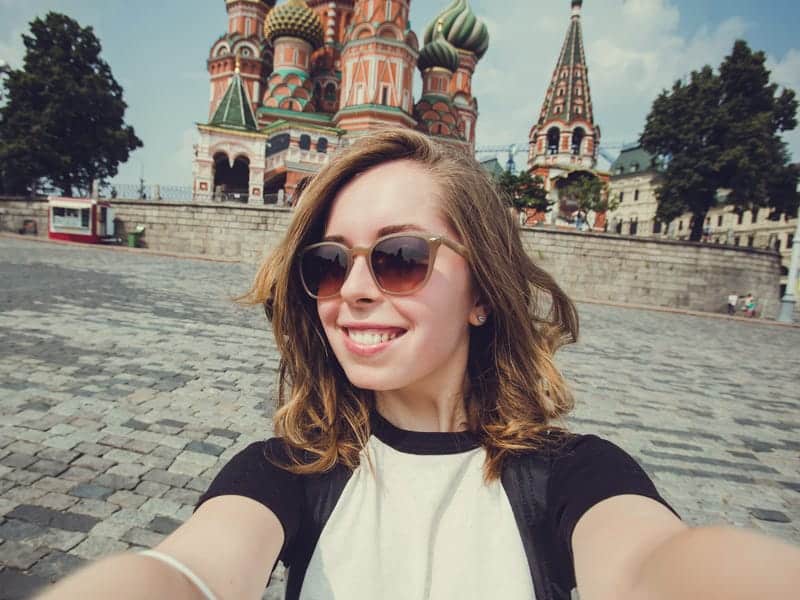 Stunning woman taking a selfie at Red Square in Moscow, Russia, with colorful St. Basil's Cathedral in the background.